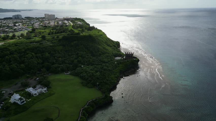 Stunning aerial overview of lush hilltop and quaint chapel overlooking ocean coast during sunset at Tamuning, Guam, USA.