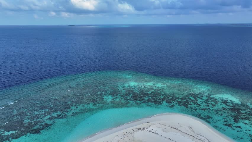 Aerial view of an island featuring a white sand beach, vibrant green trees, and turquoise waters contrasting with the deep blue sea, Maalhos, Baa Atoll, Maldives.