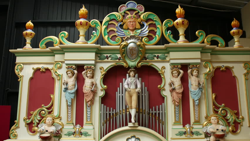 An organ with ornate wooden carvings and painted statues is standing as a decorative centerpiece. Antique pipe organ with cherubs and classical detailing is prominently featured