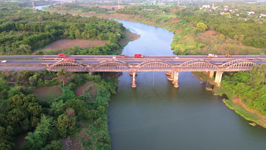Drone Shot landscape blends with infrastructure, Aerial View Expressway Bridge Over River in Lush Greenery, Calm Waters Flow Beneath Concrete Viaduct, Traffic Passes Above riverbed, Highway connects
