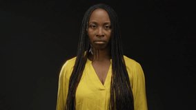 African woman wearing yellow shirt stands against a dark background, showcasing her braided hairstyle with a serious expression. - Powered by Shutterstock - Get 15% off with code: PIKWIZARD15