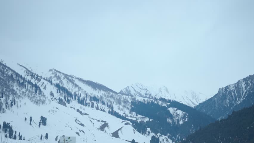 4K Landscape shot of snowy Himalayan mountain peaks during a winter storm as seen from Sonmarg in Jammu and Kashmir, India. Scenic view of snow clad mountain peaks with pine trees on top of them. 