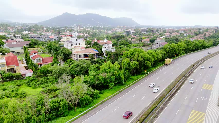 Drone shows expressway winding near suburban homes, Aerial shot of Pune Mumbai highway with cottages, Summer landscape surrounds busy travel roadways, Bright hamlet scatter across rural roadside view