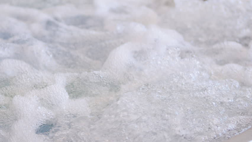Slow motion view of bubbling water and foam in a hot tub, showing dynamic movement, texture, and energy. Air jets create a relaxing, invigorating spa effect with swirling bubbles.