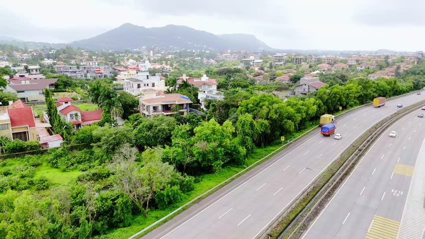 Aerial shot of Pune Mumbai highway with cottages, Drone shows expressway winding near suburban homes, Summer landscape surrounds busy travel roadways, Bright hamlet scatter across rural roadside view