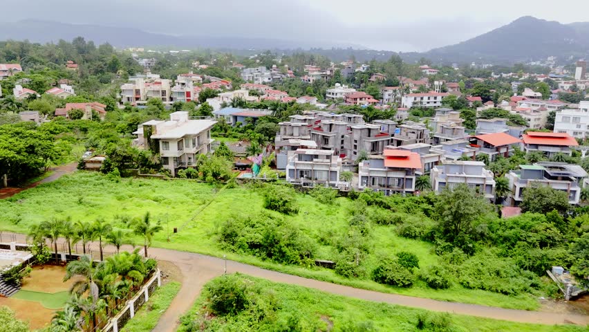 Aerial shot reveals modern dwellings by thick trees, Drone view small town aligned with leafy roads, Cottages line the edge of green valleys, Clustered chalet appear between rolling grasslands, Villas