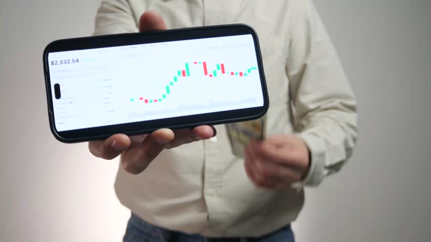 A businessmans hand triumphantly waves money while the other holds a smartphone displaying a growing financial graph and a healthy account balance. This clip is the ultimate visual metaphor for