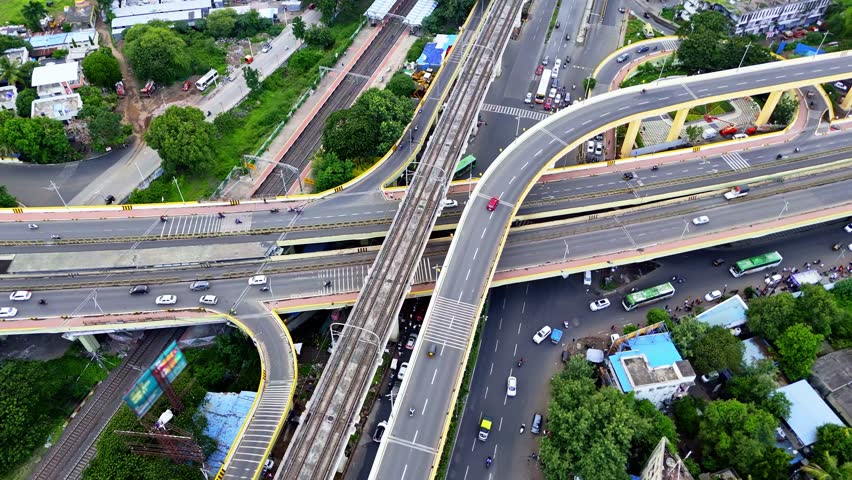 Drone shot overlapping flyover across pune metro cityscape, Aerial View multi tier bridge network in mumbai city, Busy metropolitan filled with heavy traffic, Train hub by streets and vegetation, Road