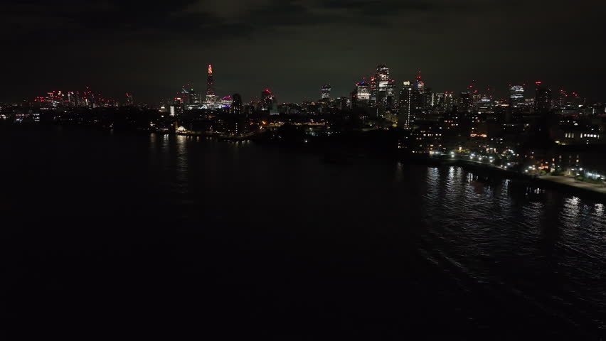 Aerial view rising over Thames river toward the illuminated London skyline, night