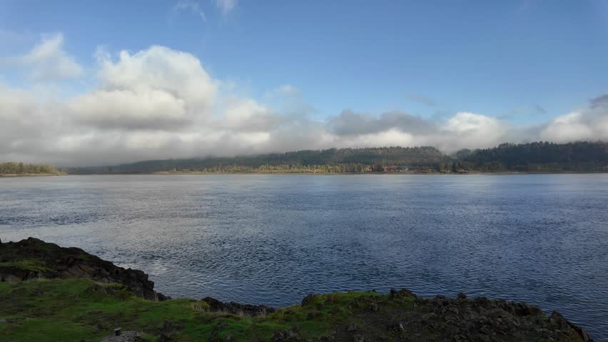 4K video of Columbia River in Oregon, USA on a calm late fall morning with misty clouds, blue sky, and distant hills. Beautiful Pacific Northwest landscape perfect for travel, nature, and roll use
