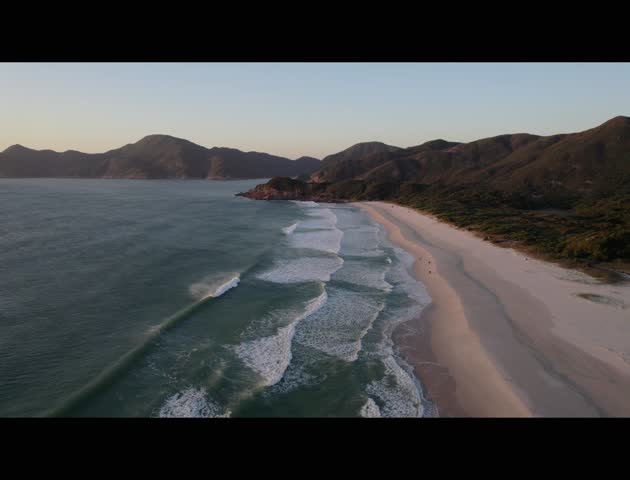 A high-angle scenic view of Tai Long Wan, Hong Kong, with white sand, rolling waves, and green mountains along the undeveloped coastline