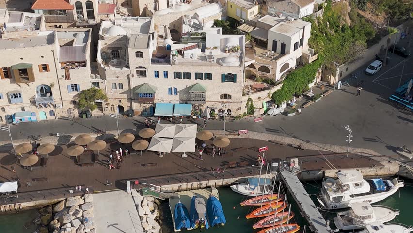 Aerial view of buildings with umbrellas and boats along the shore, creating a harmonious blend of urban and coastal elements, Old Jaffa, Tel Aviv-Yafo, Israel.