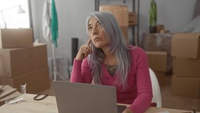 Senior woman with grey hair working on a laptop in a new home living room surrounded by moving boxes, creating an atmosphere of transition and new beginnings. - Powered by Shutterstock - Get 15% off with code: PIKWIZARD15