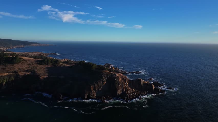 Aerial view of the dramatic cliffside coastline where the golden land meets the deep blue sea under a clear sky, California, California, United States.