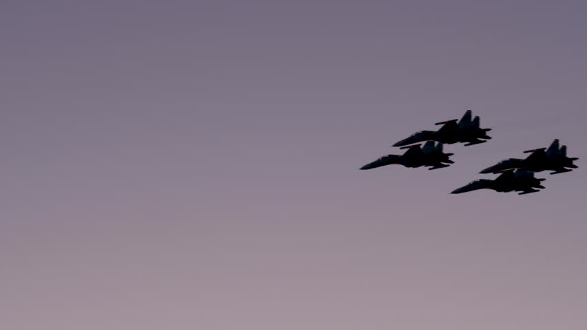 Four military fighter jets flying in a synchronized formation, silhouetted against the colorful sky during a beautiful sunset, performing maneuvers. Patriotic airshow demonstration