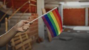 Hand holding lgbt rainbow flag in indoor construction site setting with background of brick and concrete. - Powered by Shutterstock - Get 15% off with code: PIKWIZARD15