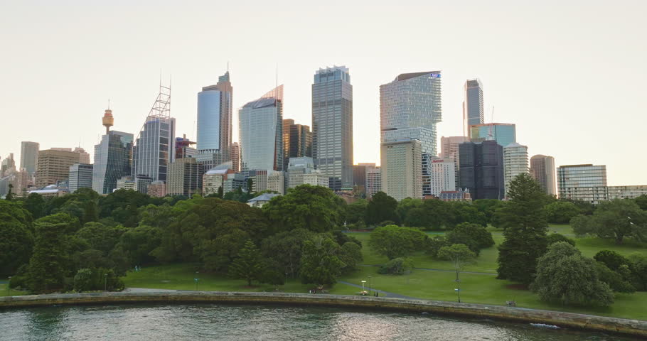 Australia, Sydney: Sydney's modern skyline, highlighted by iconic Sydney Tower, rises above the lush Royal Botanic Garden, creating a stunning contrast during a vibrant sunset. Drone flight footage