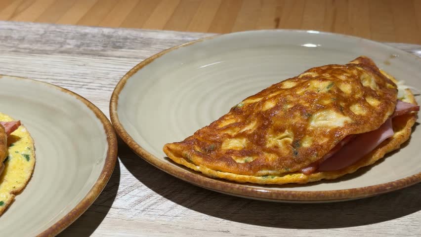 Omelette filled with ham served on ceramic plates on wooden table video
