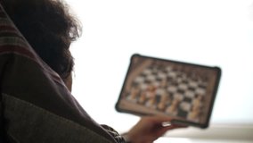 Elderly woman interacts with digital chess game on tablet while seated indoors near bright window. - Powered by Shutterstock - Get 15% off with code: PIKWIZARD15
