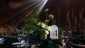 Luxury wedding reception. Festive table setting with flower arrangement, number 4 for guests on black tablecloth, green napkins, candles on backdrop, soft moving searchlight rays in hall restaurant. - Powered by Shutterstock - Get 15% off with code: PIKWIZARD15