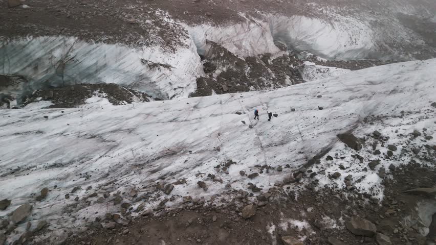 Two tiny figures walk across the Mer de Glace glacier in the French Alps near Chamonix in the Mont Blanc massif.