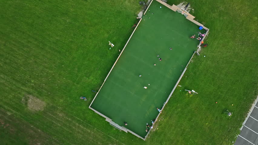 Aerial top-down video of Vinni, Estonia. Outdoor sports field near Vinni Sports Center with children playing football surrounded by green grass, bikes, and local activity.
