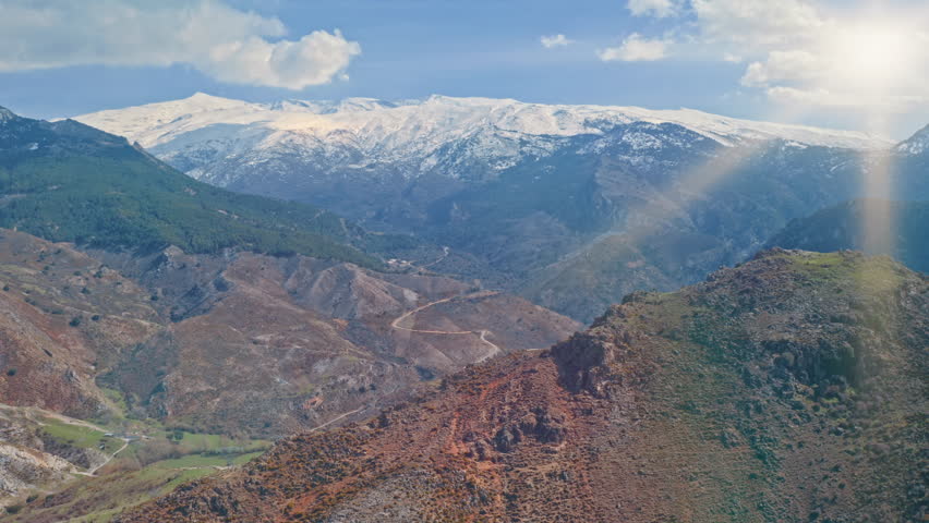 Ancient Sierra Nevada highlands of Andalusia with snow covered peaks red earth valleys traces of moorish heritage routes and golden sun rays illuminating timeless traveling touristic mountains roads