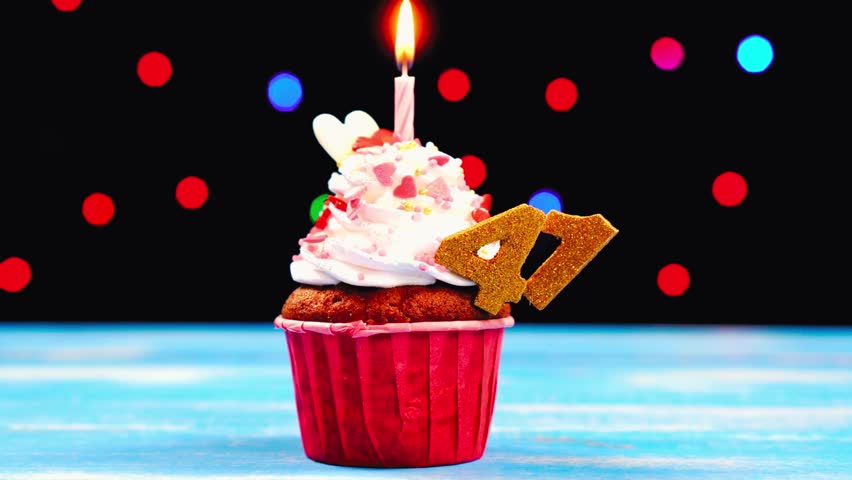 Delicious birthday cupcake with a burning candle and number 41 topper — glowing beautifully against a multicolored blurred lights background for a joyful celebration scene.