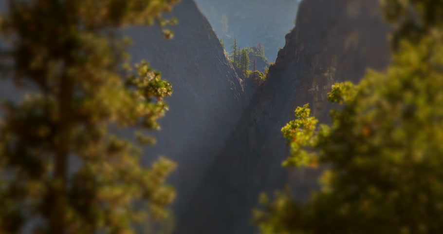 A cinematic daytime timelapse of sunlight glowing across a granite crevice in Yosemite National Park, California. Trees and cliffs create a natural V-shaped composition in soft focus.
