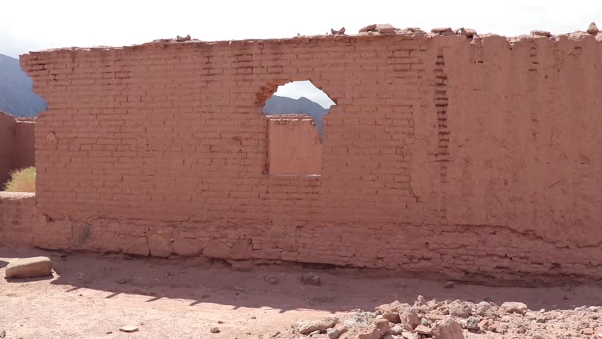 A decaying adobe wall at the Mayorazgo ruins in Anillaco, Catamarca. Eroded window aperture framing the distant mountains and arid landscape.