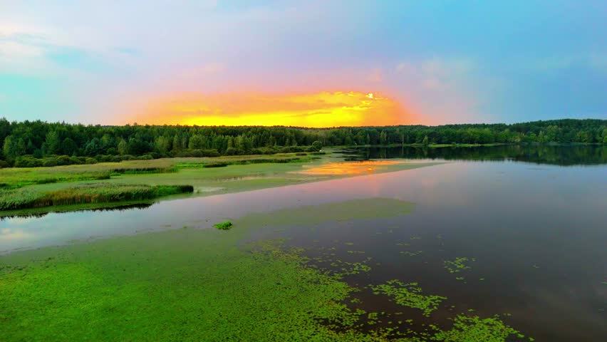 Drone view of calm lake reflecting vibrant sunset sky, peaceful natural summer landscape.