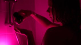 Young woman pouring shampoo into hand and foaming hair with her hands under pink neon shower light, self care moment, washing hair and relaxing - Powered by Shutterstock - Get 15% off with code: PIKWIZARD15