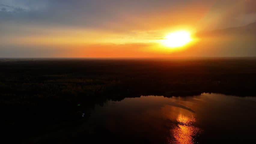 Drone aerial view of sunset over river, warm light reflecting on water, peaceful nature landscape.