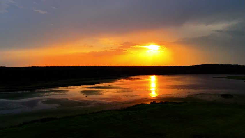 Drone aerial view of sunset over wetlands, golden reflections on calm water, tranquil summer landscape.