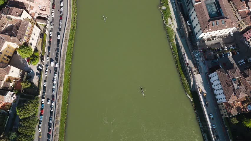 Top-down drone view of the Arno River, with rowers gliding across the water between Florence’s riverbanks.