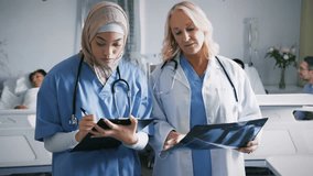 Younger doctor tapping tablet activating patient metrics while senior doctor pointing X-ray details. Medical team, healthcare technology, digital diagnostics, clinical collaboration, modern hospital, - Powered by Shutterstock - Get 15% off with code: PIKWIZARD15