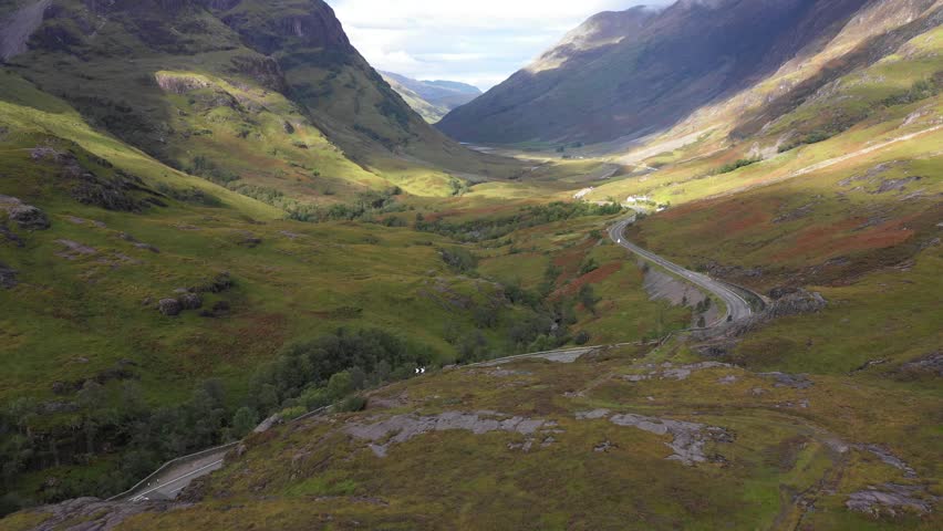 Scenic drone view of a road winding through highlands in Scotland near Glencoe - Nature and travel concepts with the Three Sisters of Glencoe mountains on the left on a beautiful day