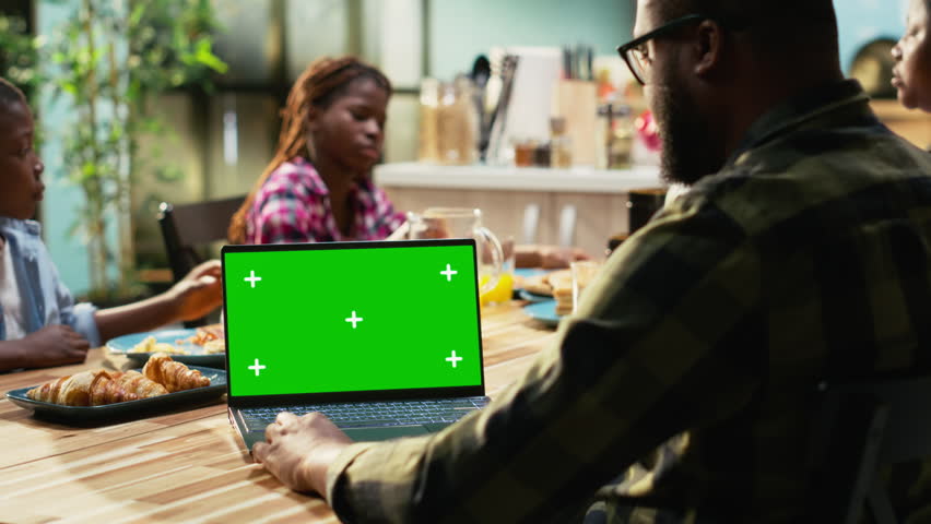 Chroma key next to black family enjoying breakfast at the kitchen table, with plates of omelettes, toast and fruits. Parents and kids laugh together, starting the day with delicious food. Camera B.
