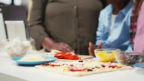 Black family prepares homemade pizza by adding grated cheese and ingredients in cozy kitchen. Parents and children sharing joy and laughter during this fun weekend cooking activity. Camera B. - Powered by Shutterstock - Get 15% off with code: PIKWIZARD15