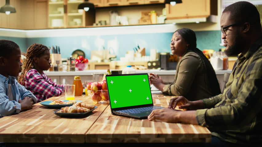 Mockup screen with African American family gathered for breakfast in the kitchen. Parents serve milk and orange juice while children enjoy granola and fruit, homemade meal at home. Camera A.