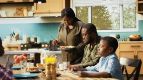 Parents and kids sitting together at breakfast table being served by the mother, serving omelette with bacon and goods. Cozy scene captures family bonding with joy for morning routine. Camera B. - Powered by Shutterstock - Get 15% off with code: PIKWIZARD15