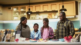 Black family prepares homemade pizza by adding grated cheese and ingredients in cozy kitchen. Parents and children sharing joy and laughter during this fun weekend cooking activity. Camera A. - Powered by Shutterstock - Get 15% off with code: PIKWIZARD15