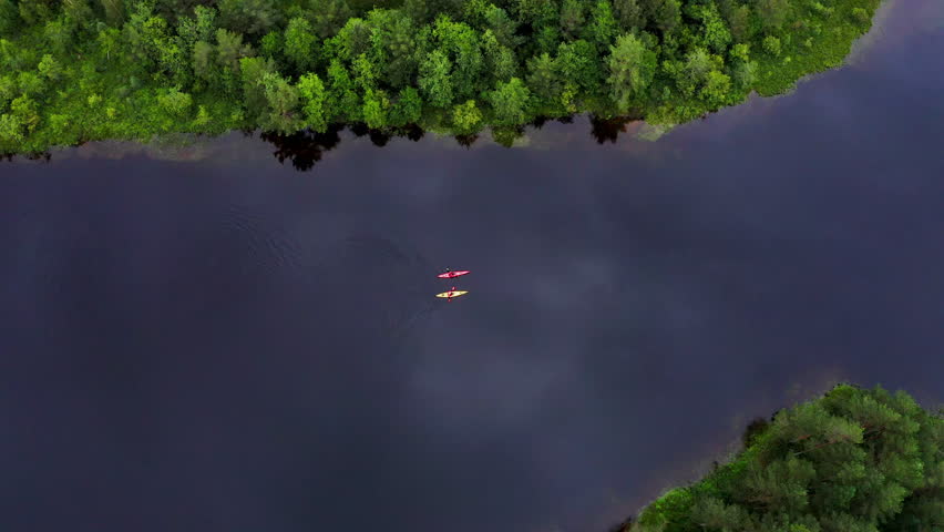 Top aerial 4K footage of yellow and red kayaks with two persons paddling kayak floating by mountain lake surrounded pine trees forest in Norway. Active people, traveling, beauty in Nature concept
