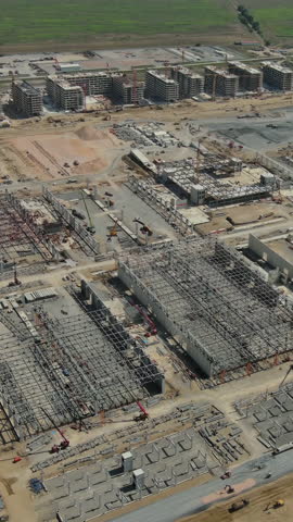 Aerial around view of large industrial construction site with construction equipment and materials. Vertical video 4k