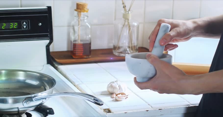 Hands pressing pestle on garlic in mortar for cooking, generating purple light streak. Culinary, food preparation, kitchenware, modern, lifestyle, vibrancy, activity