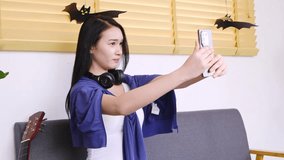 Young woman taking selfie at home with headphones and guitar in the background, autumn decor featuring paper bats on window sill - Powered by Shutterstock - Get 15% off with code: PIKWIZARD15