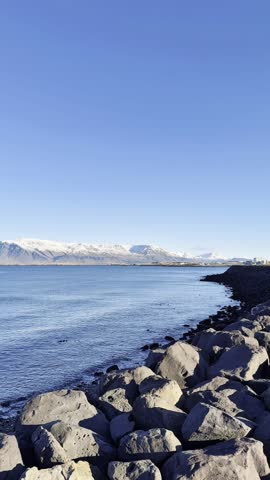 Scenic view of Reykjavík, Iceland, featuring Mount Esja and Faxaflói Bay, where the city meets icy mountains and the calm sea, capturing the serene beauty of urban life surrounded by nature.