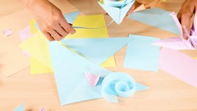 Person creates pastel origami flowers using colored paper on wooden table, top-down view, bright lighting - Powered by Shutterstock - Get 15% off with code: PIKWIZARD15
