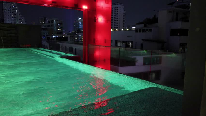 Neon-lit rooftop infinity pool with city skyline, night setting, steady camera, vibrant reflections, Bangkok