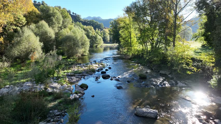 Slow drone flight upstream along the Ter River in Girona, Spain, gliding through the calm waterway under warm autumn light and golden foliage.